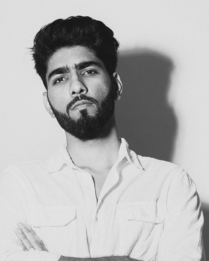 Black and white portrait of Ravinder Kumar, arms folded, in a white shirt