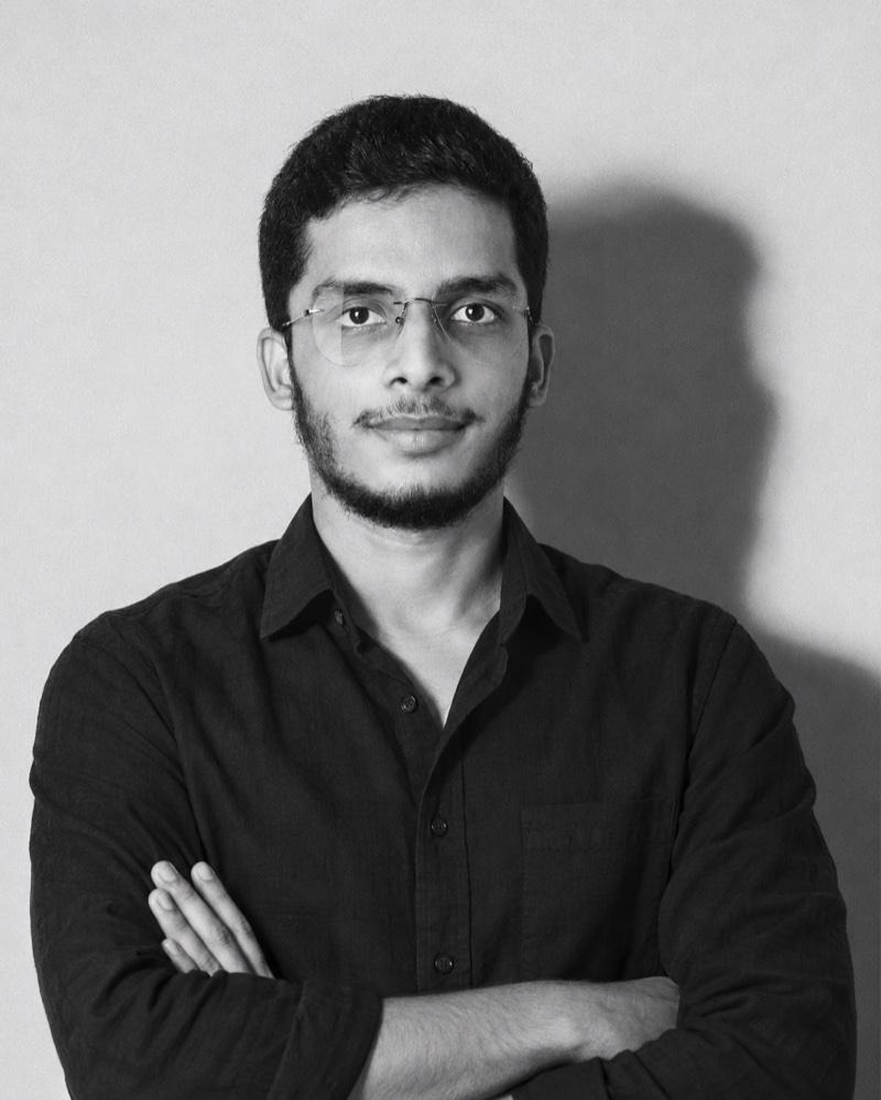 Black and white portrait of Sayed Zaid, arms folded, in a black shirt and glasses